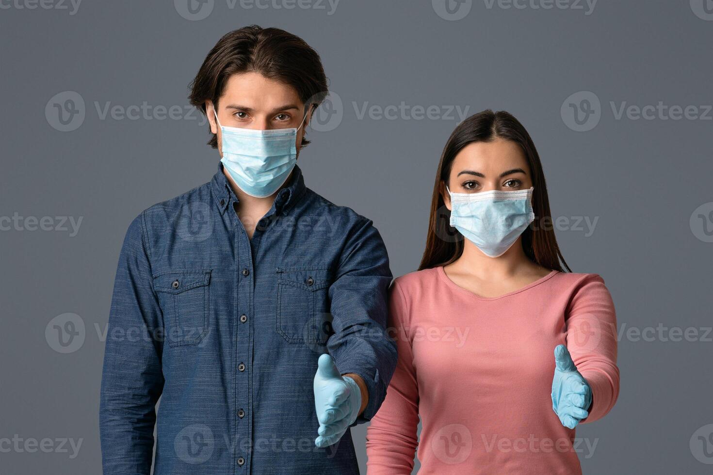 Helping Hand. Young Couple In Protective Masks And Gloves Extending Arms For Handshake At Camera Over Light Studio Background, Free Space photo