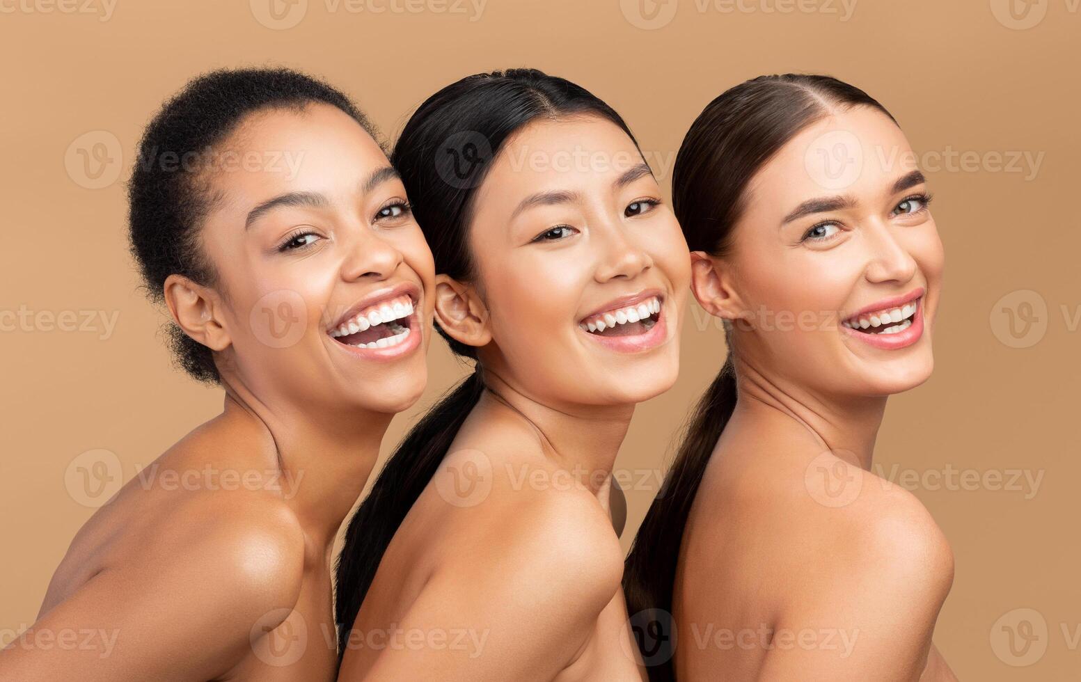 Three Diverse Ladies Models Smiling To Camera Posing Over Beige Background. Studio Shot photo