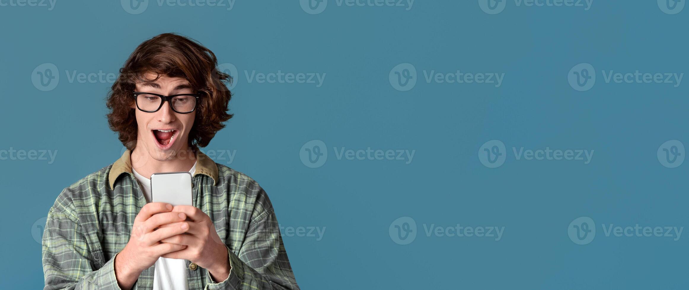Victory and success concept. Shocked millennial guy with mobile phone screaming OMG on color background photo
