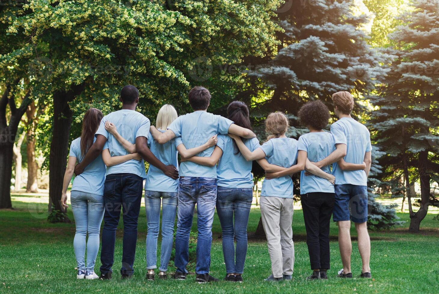 Volunteering, people and ecology concept. Group of volunteers embracing in park, back view, copy space photo