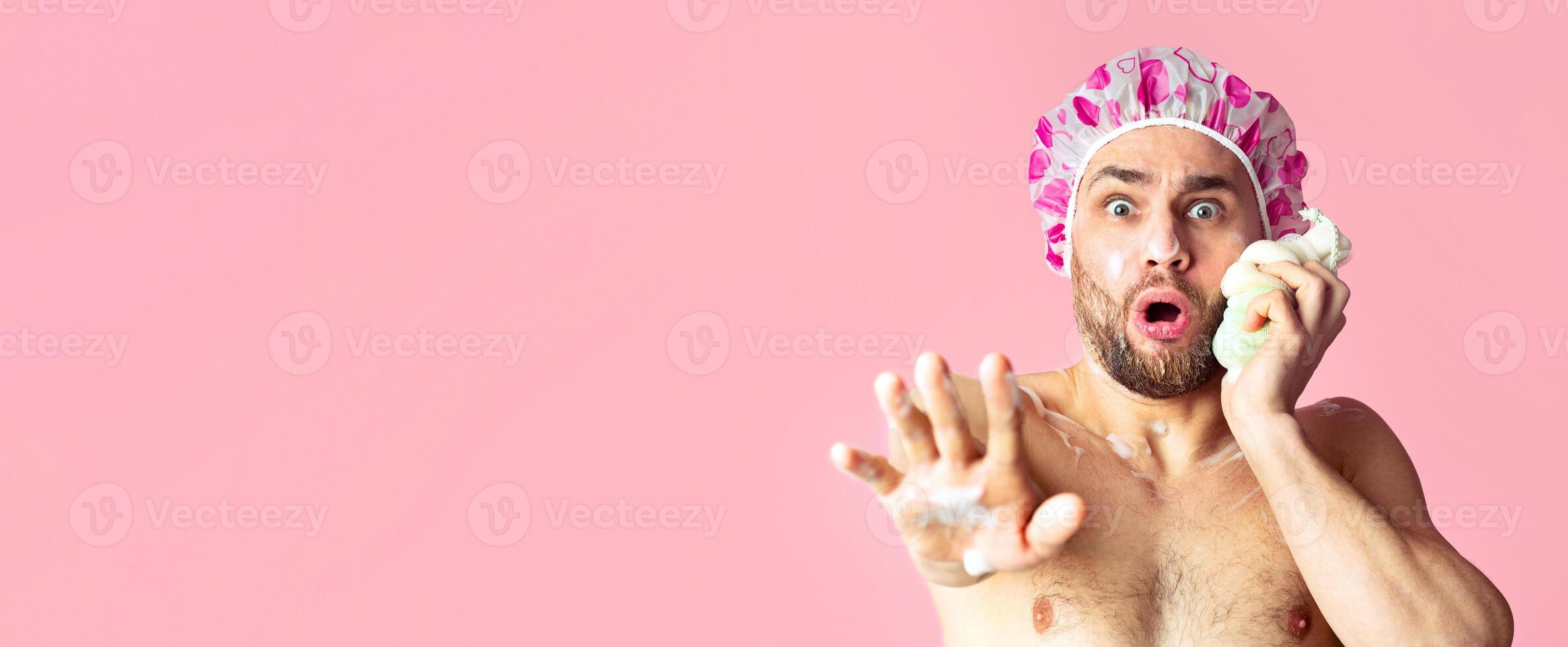 Someone came to shower. Scared guy in shower cap rubs his face with sponge photo