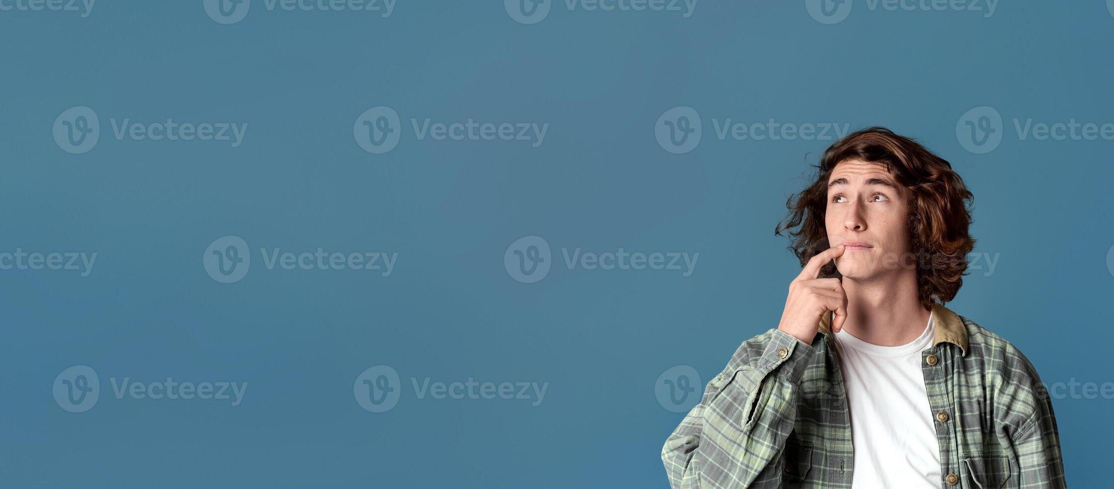 Thoughtful young guy pondering over idea on turquoise background, copy space. Panorama photo