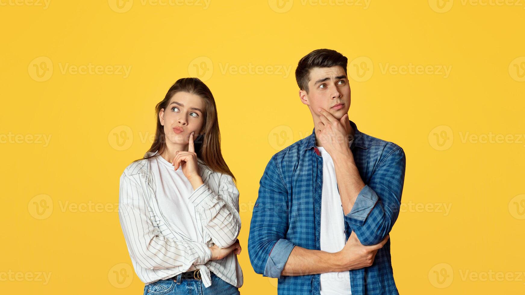 Make decision, new proposal and think about different things. Pensive young couple of students in love press their hands to faces and look at empty space, isolated on yellow background, studio shot photo