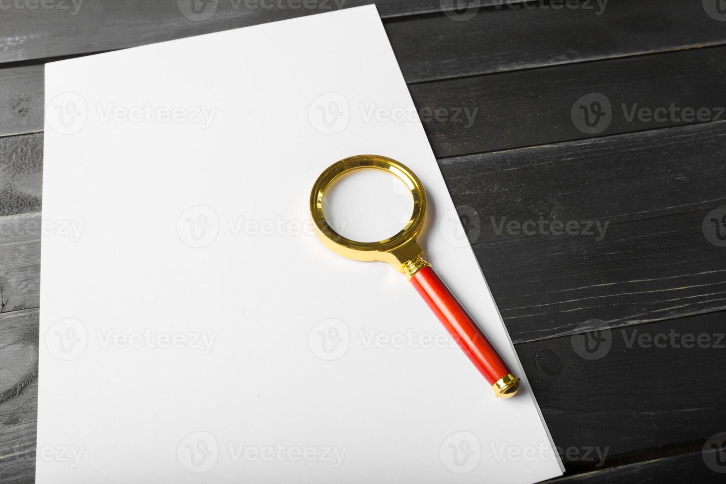 Magnifying glass and blank paper on wooden table photo