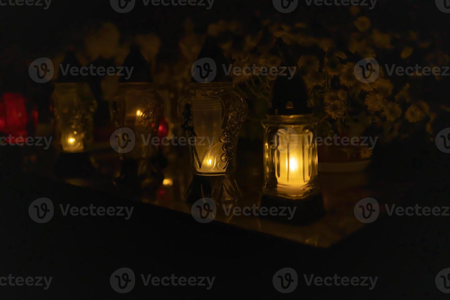 Candle lights on graves and tombstones at a cemetery in Poland during All Saints Day, Zaduszki day, and Day of the Dead. Lit candles illuminate the graves at a Christian cemetery at night. photo