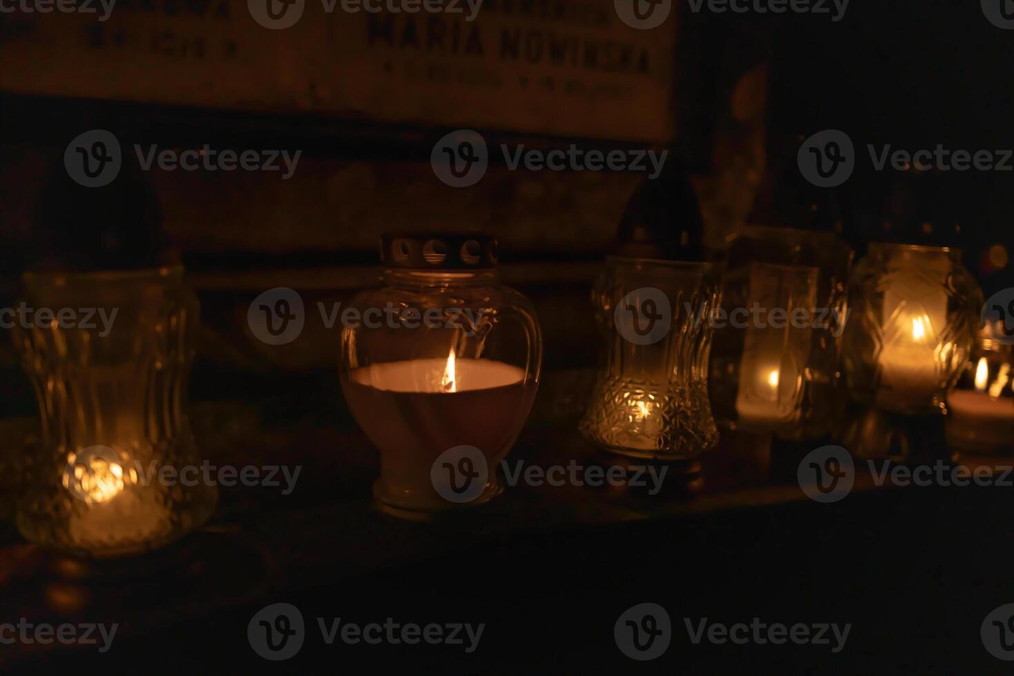 Candle lights on graves and tombstones at a cemetery in Poland during All Saints Day, Zaduszki day, and Day of the Dead. Lit candles illuminate the graves at a Christian cemetery at night. photo