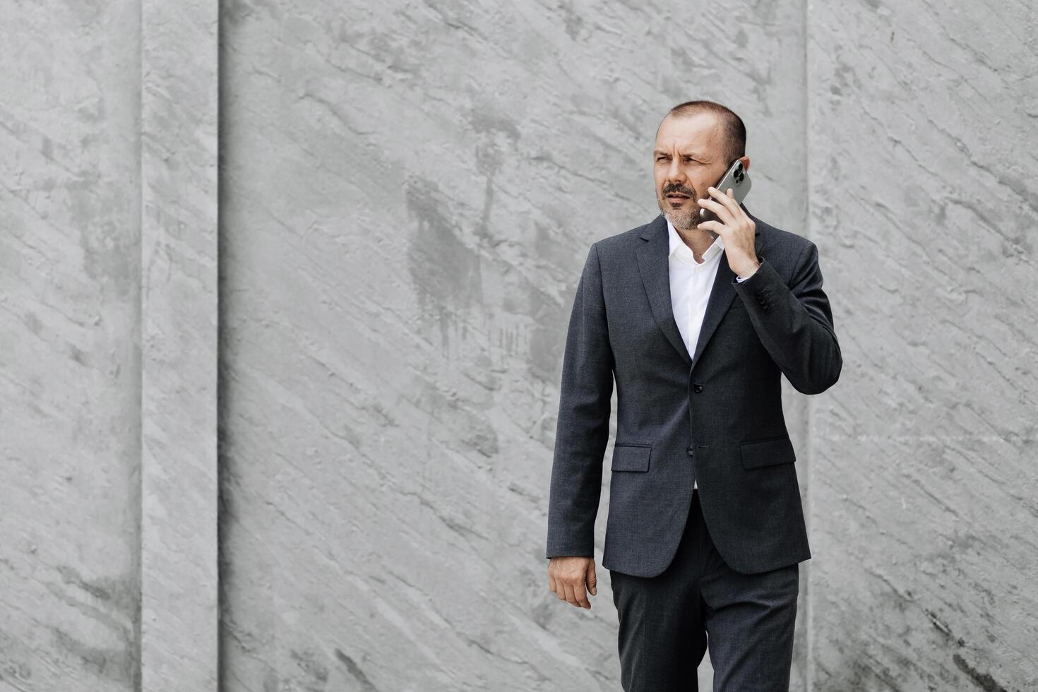 A businessman stands by a modern office talking on the phone, receiving joyful news about a deal completion. Confidence and success in business are evident on his face photo