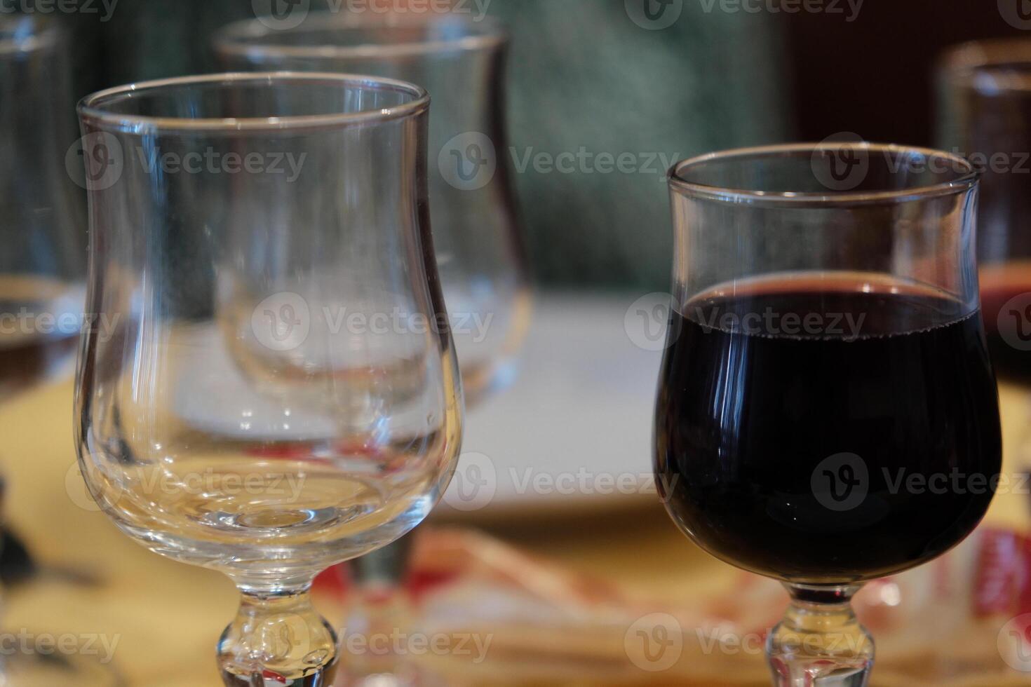 two glass wine glasses. one full of red wine, the other empty. in a bar where people are drinking photo