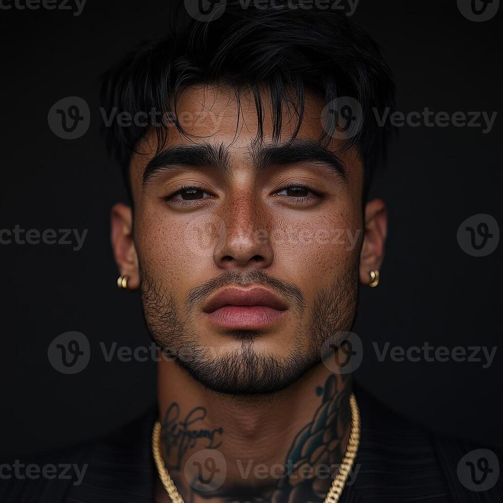 Portrait of a young man with tattoos and gold accessories in a dark setting photo
