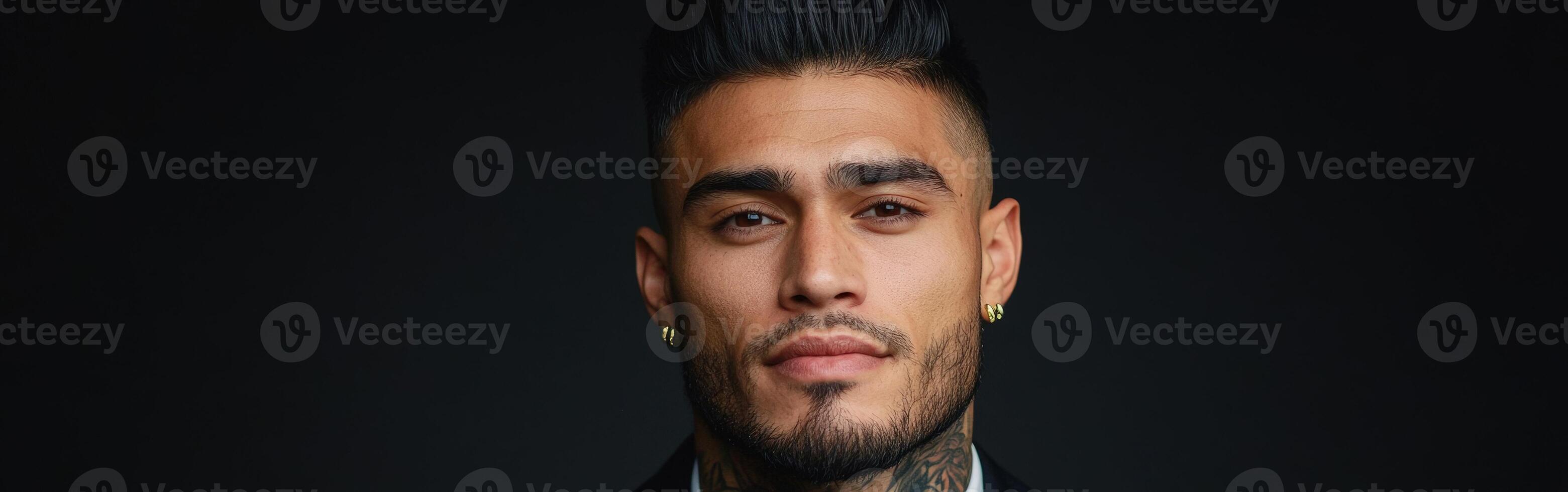 Stylish young man with tattoos poses confidently against a dark background photo