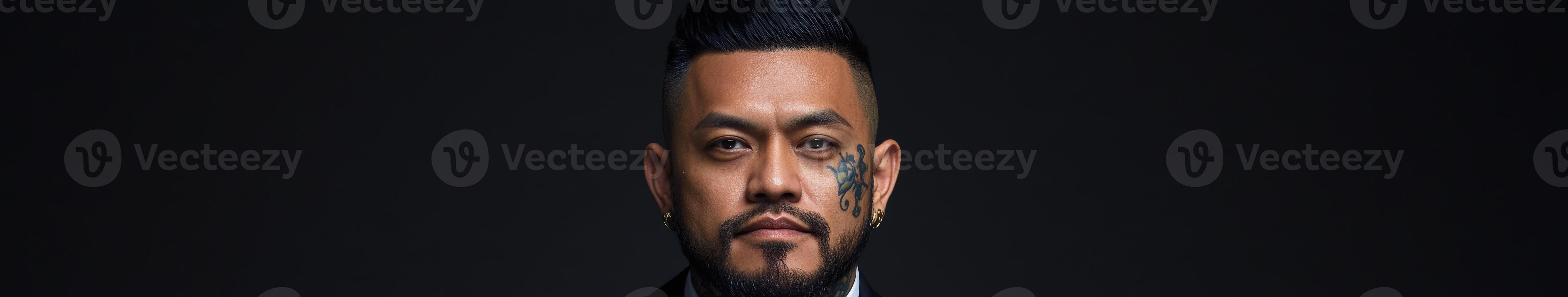 Man with a defined beard and facial tattoo posing against a dark background photo