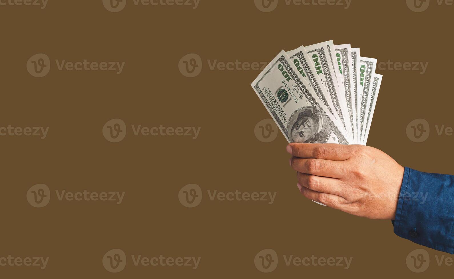 Close-up of hand holding US banknotes while standing in the studio with a brown background photo