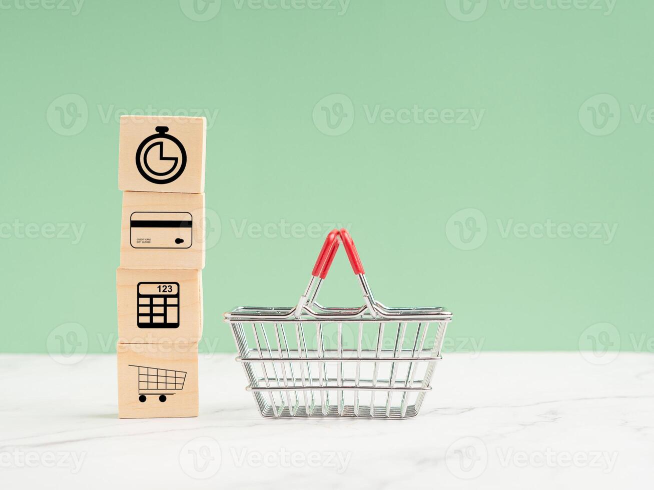 Wooden cubes with icons of the time, a credit card, a calculator, a shopping trolley. A shopping basket over a marble floor against a light green background photo