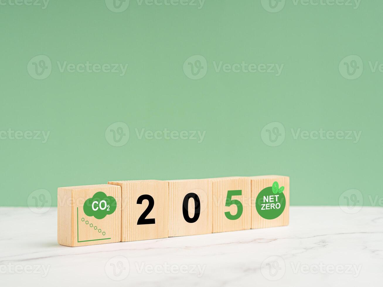 Net-zero greenhouse gas emissions target. Wooden cubes with green icons over a marble floor against a light green background photo
