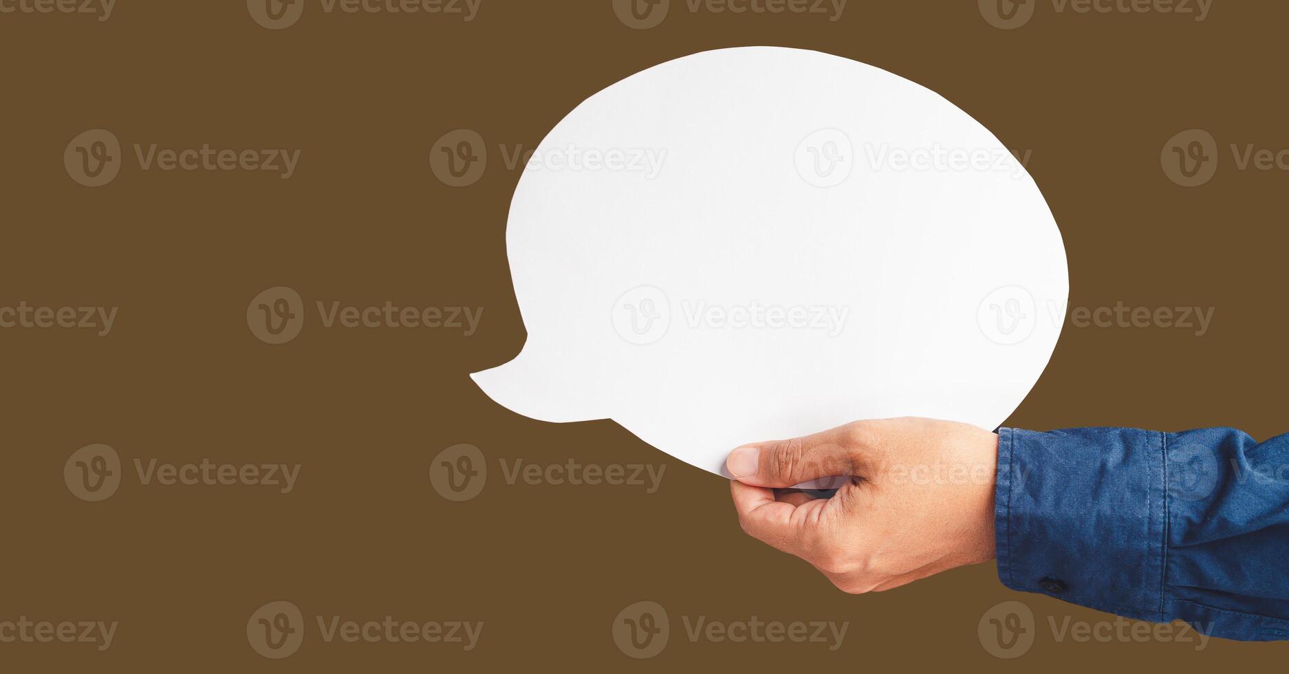 Close-up of hand holding a white speech bubble against a brown background photo
