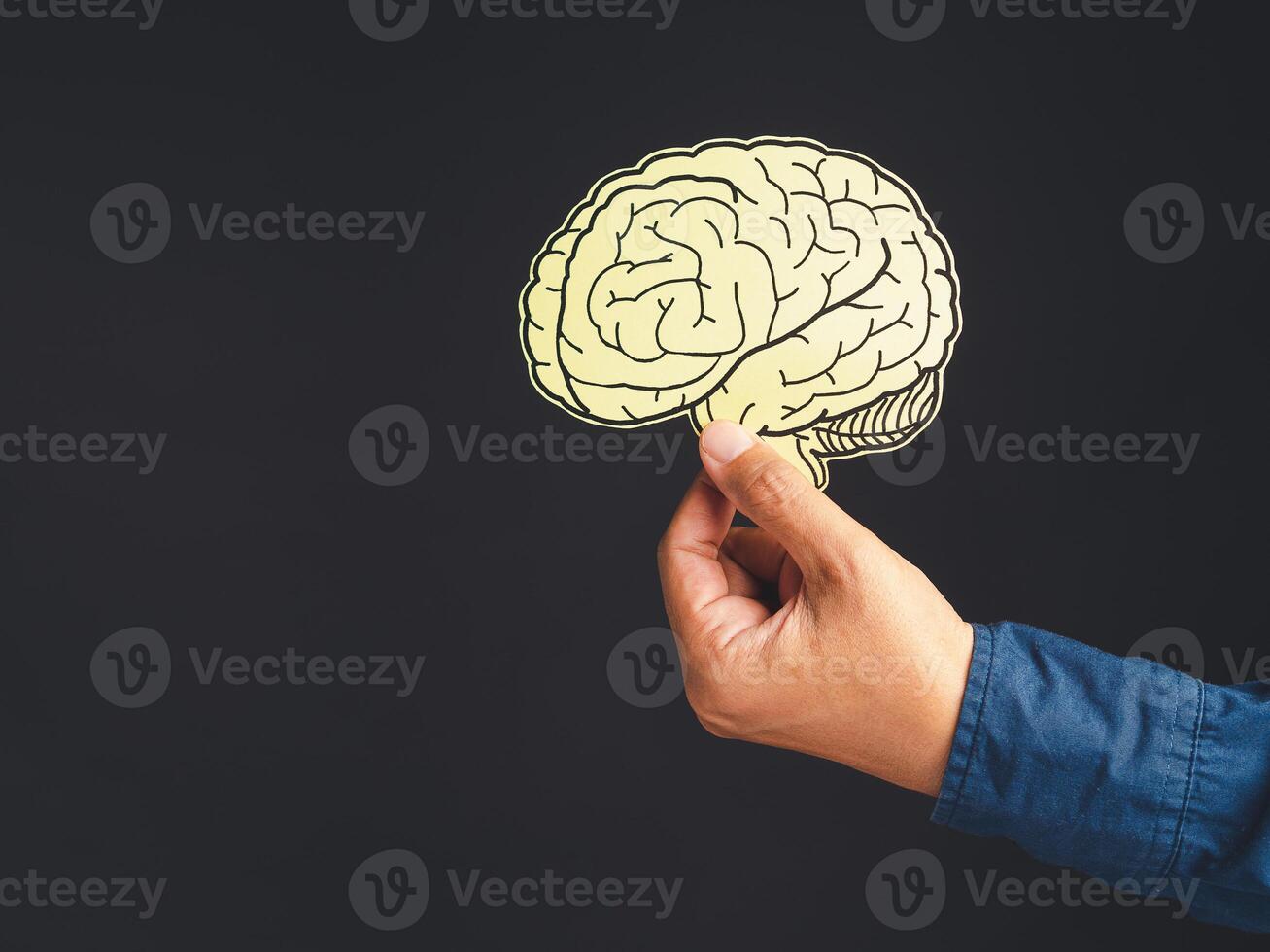 Close-up of hand holding a brain shape made from yellow paper standing against a black background photo