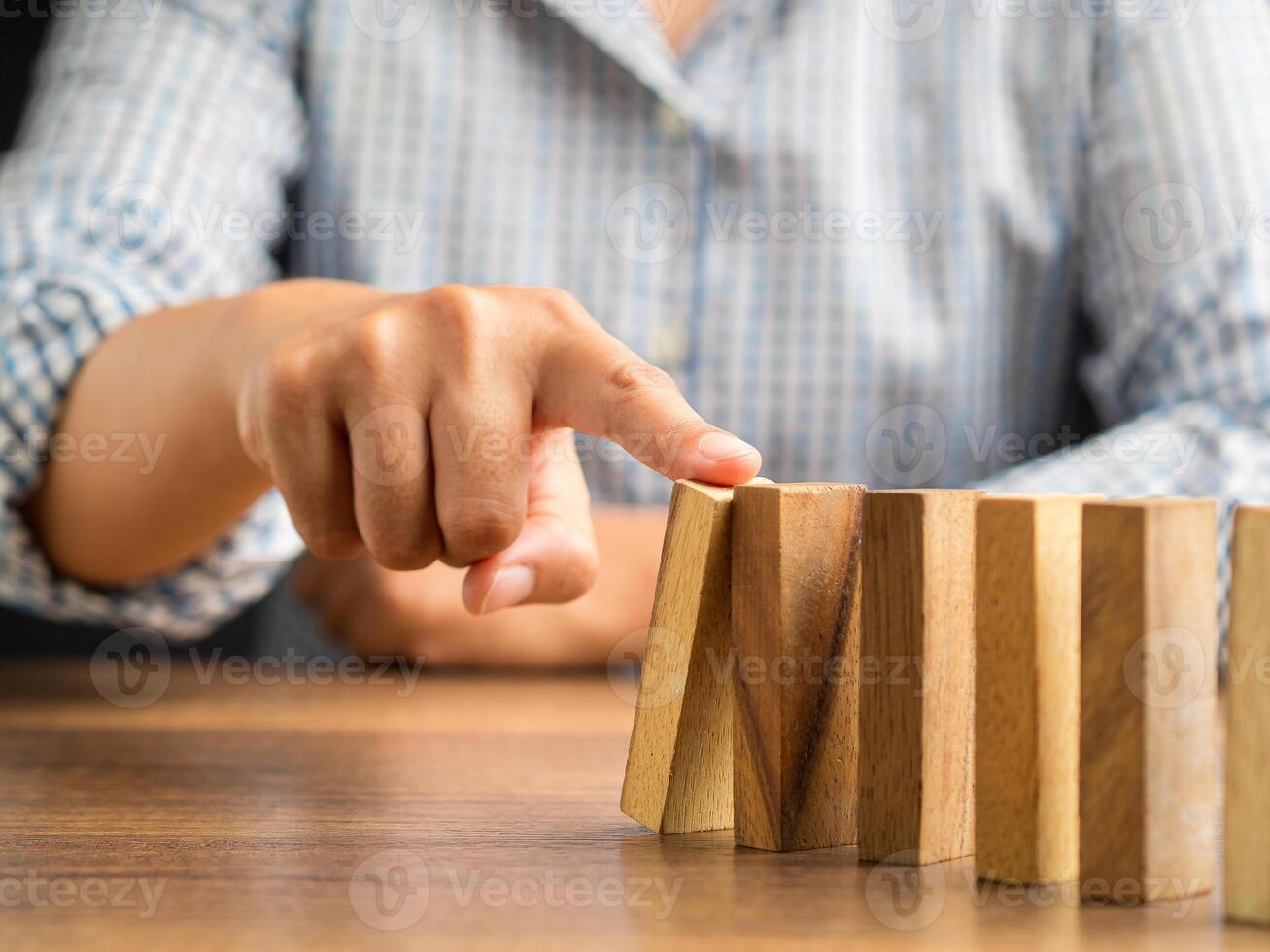 Risk and strategy in business concept. Close-up of hand pushing a wooden block on a line of dominos while sitting in the office photo