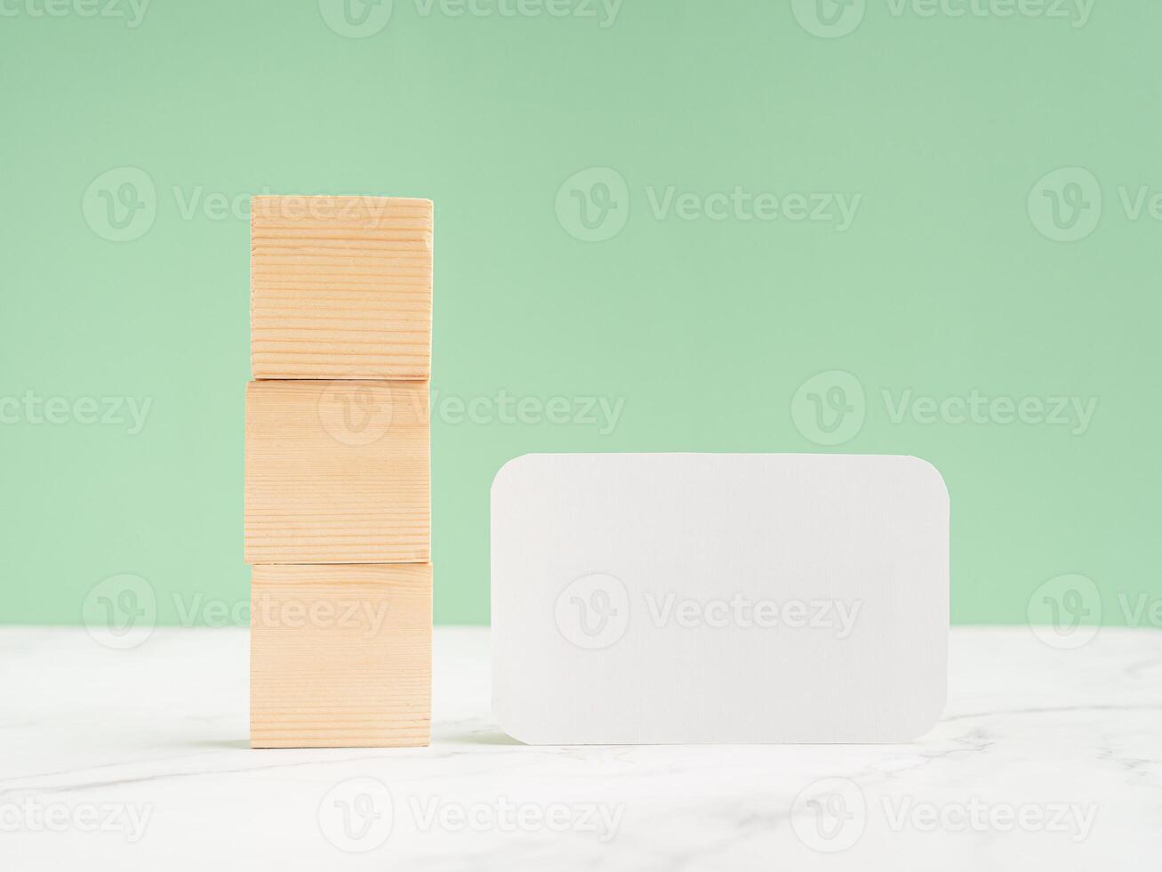 Three blank wooden cubes and a blank white paper on a marble floor against a light green background photo