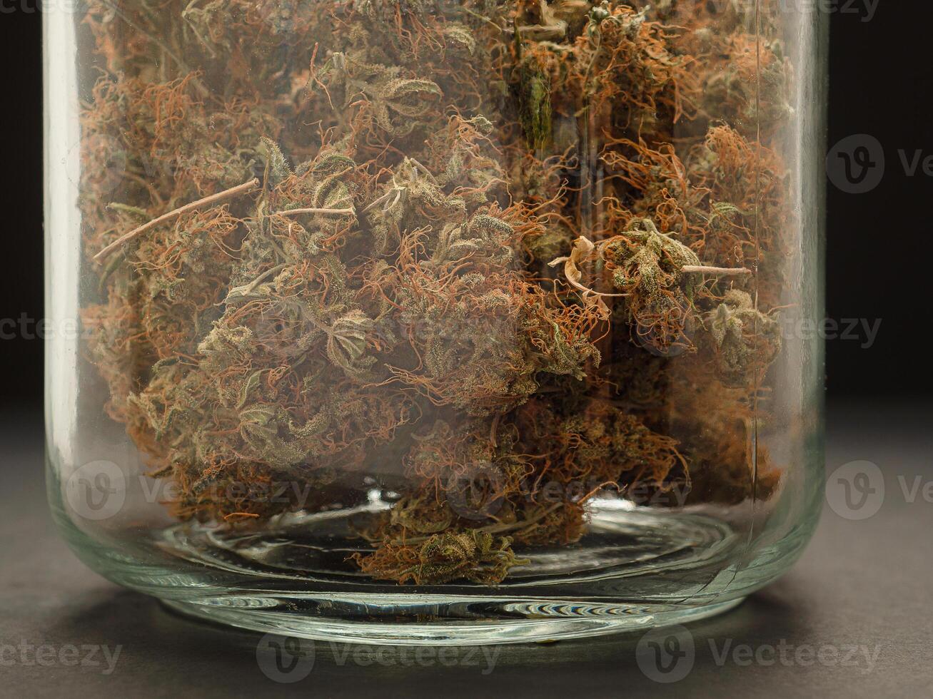 Dry cannabis buds flower in a jar glass on the table with a black background photo