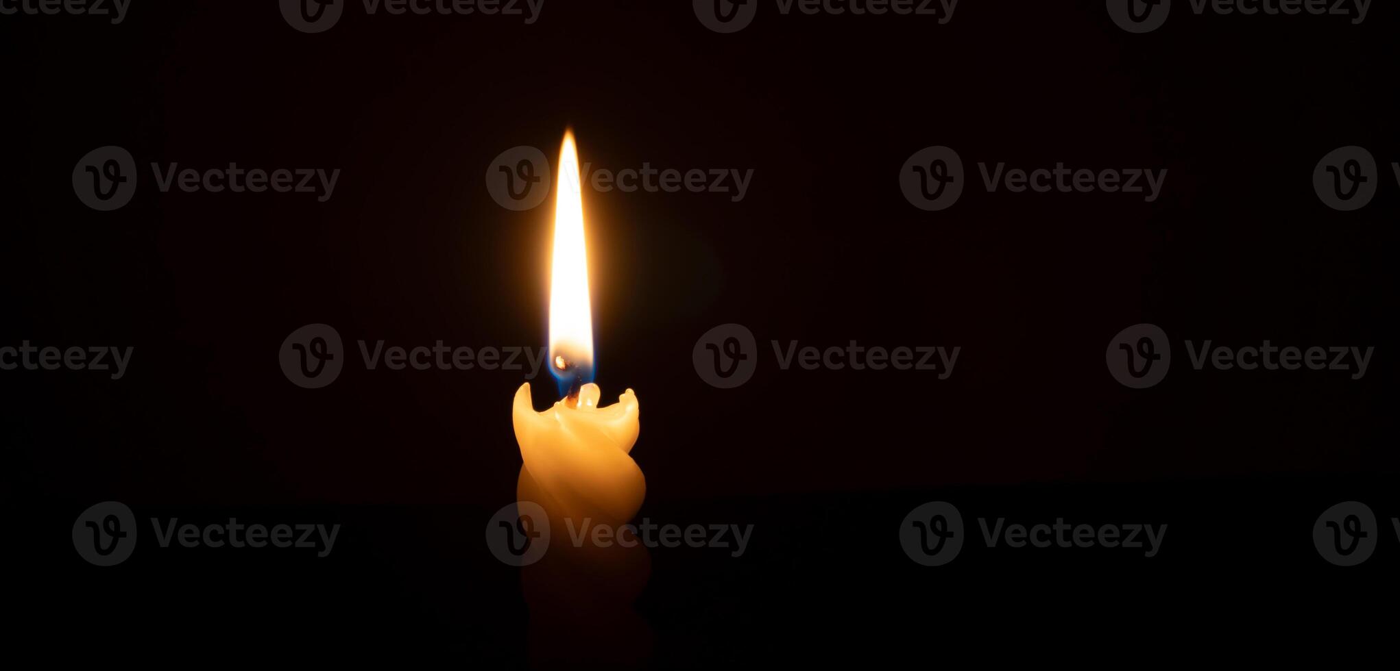 A single burning candle flame or light glowing on a spiral white candle on black or dark background on table in church for Christmas, funeral or memorial service with copy space photo