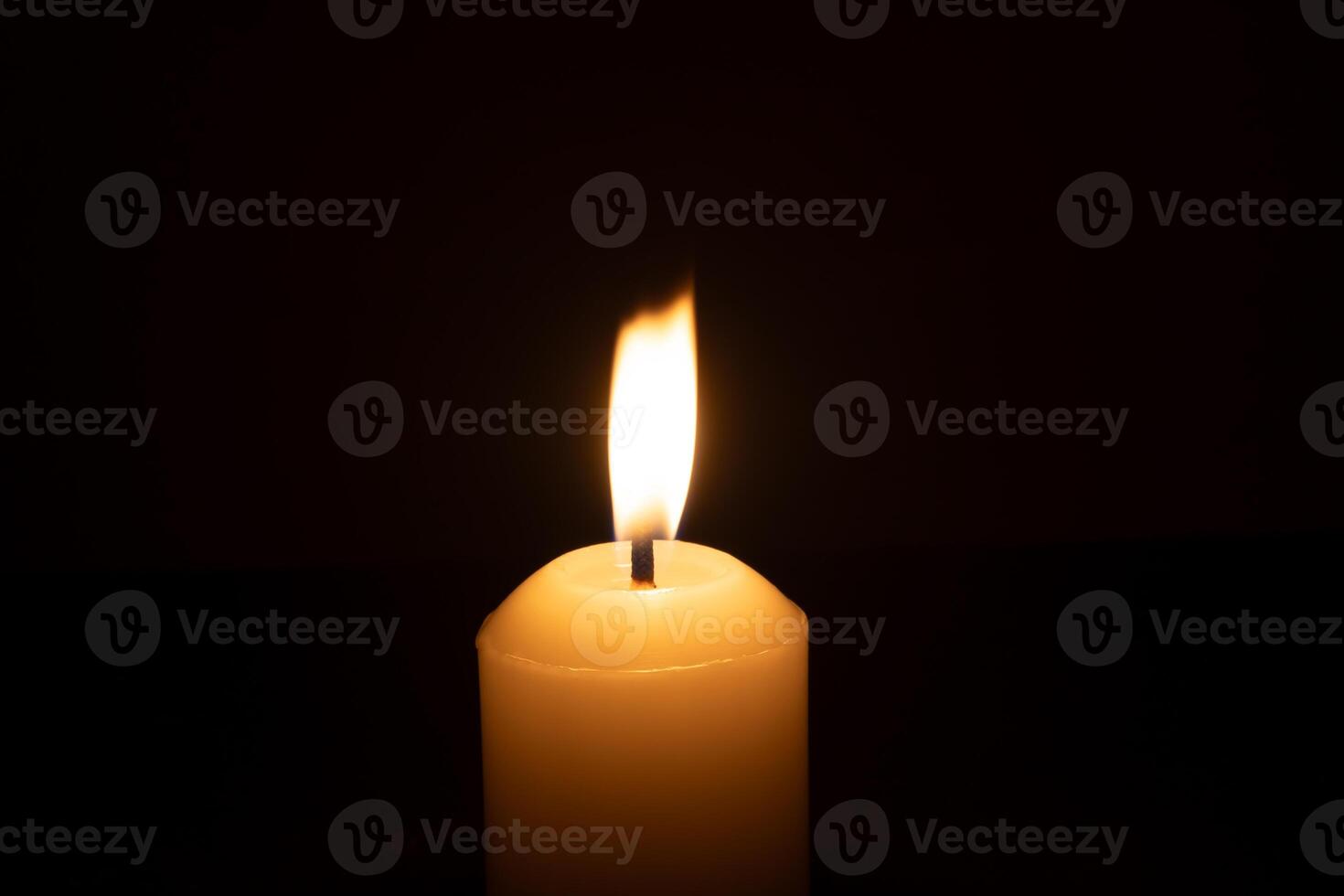 A single burning candle flame or light glowing on a big white candle isolated on red or dark background on table in church for Christmas, funeral or memorial service photo