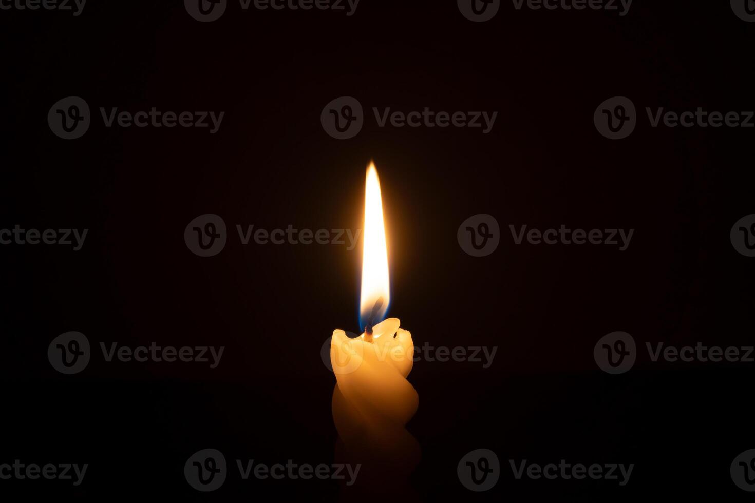 A single burning candle flame or light glowing on a spiral white candle on black or dark background on table in church for Christmas, funeral or memorial service with copy space photo