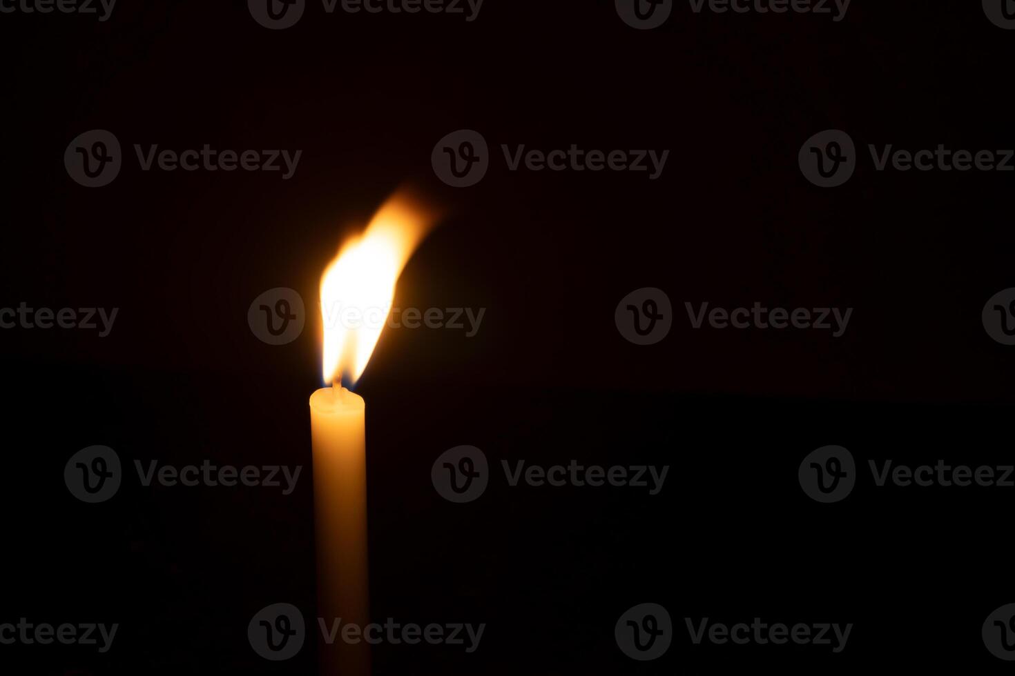 A single burning candle flame or light glowing on a small orange candle on black or dark background on table in church for Christmas, funeral or memorial service with copy space photo