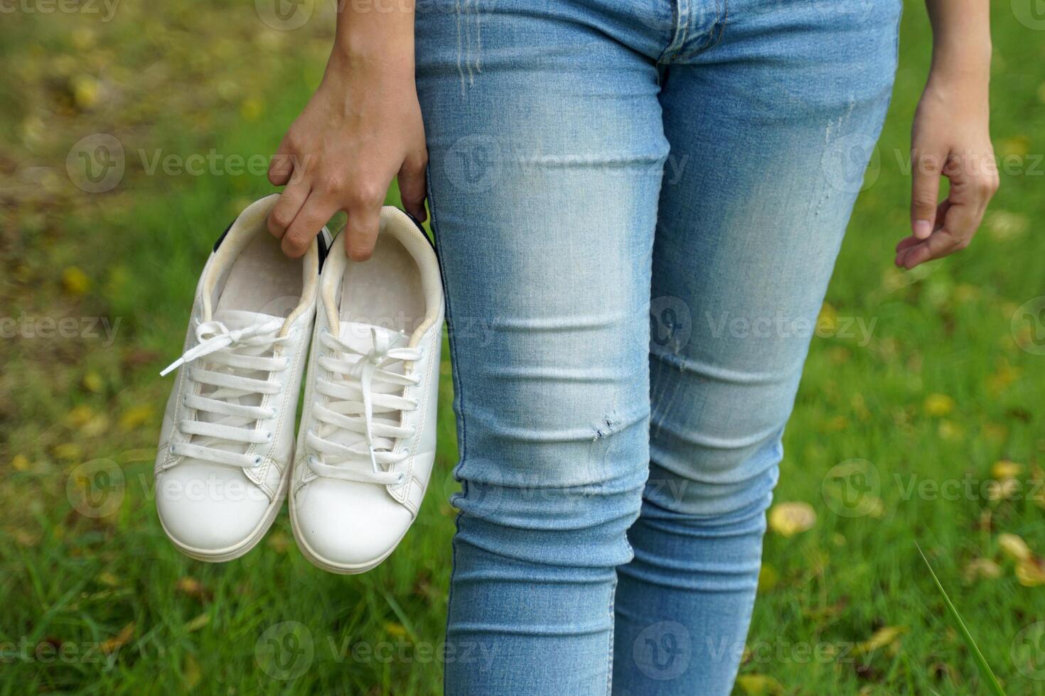 Young Asian woman takes off her shoes and walks barefoot on the grass. His right hand holds a pair of white sneakers. photo