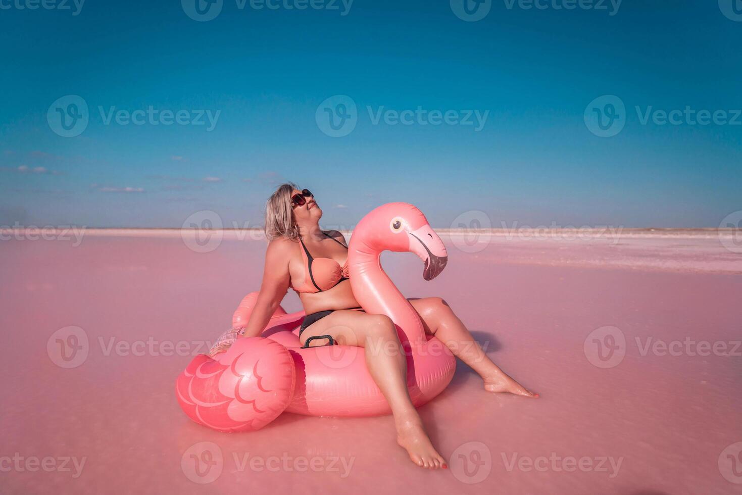 Pink Lake Flamingo Float Summer Vacation - Woman enjoys summer vacation on a pink inflatable flamingo float in a pink lake. photo