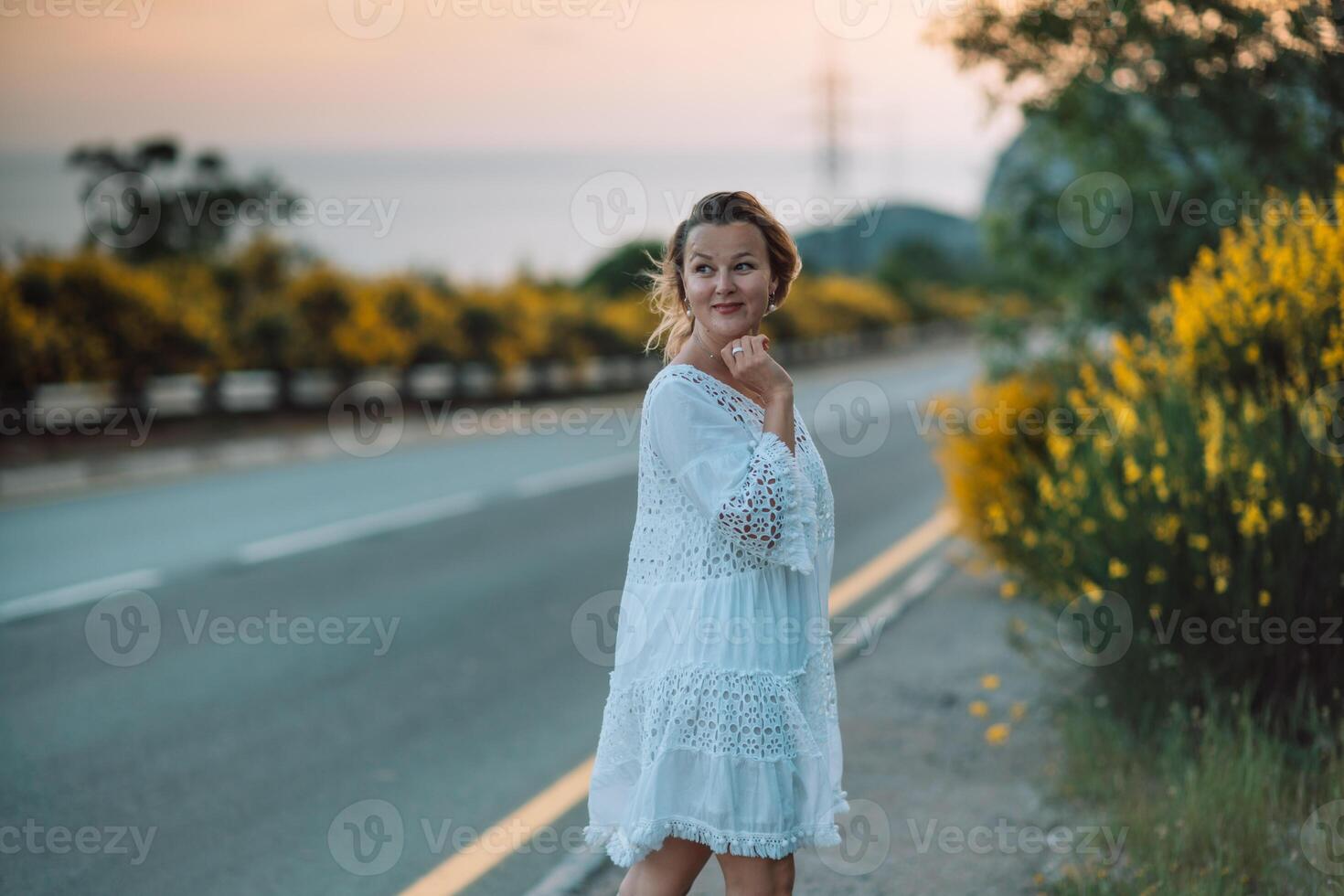 A woman in a white dress is standing on the side of a road photo