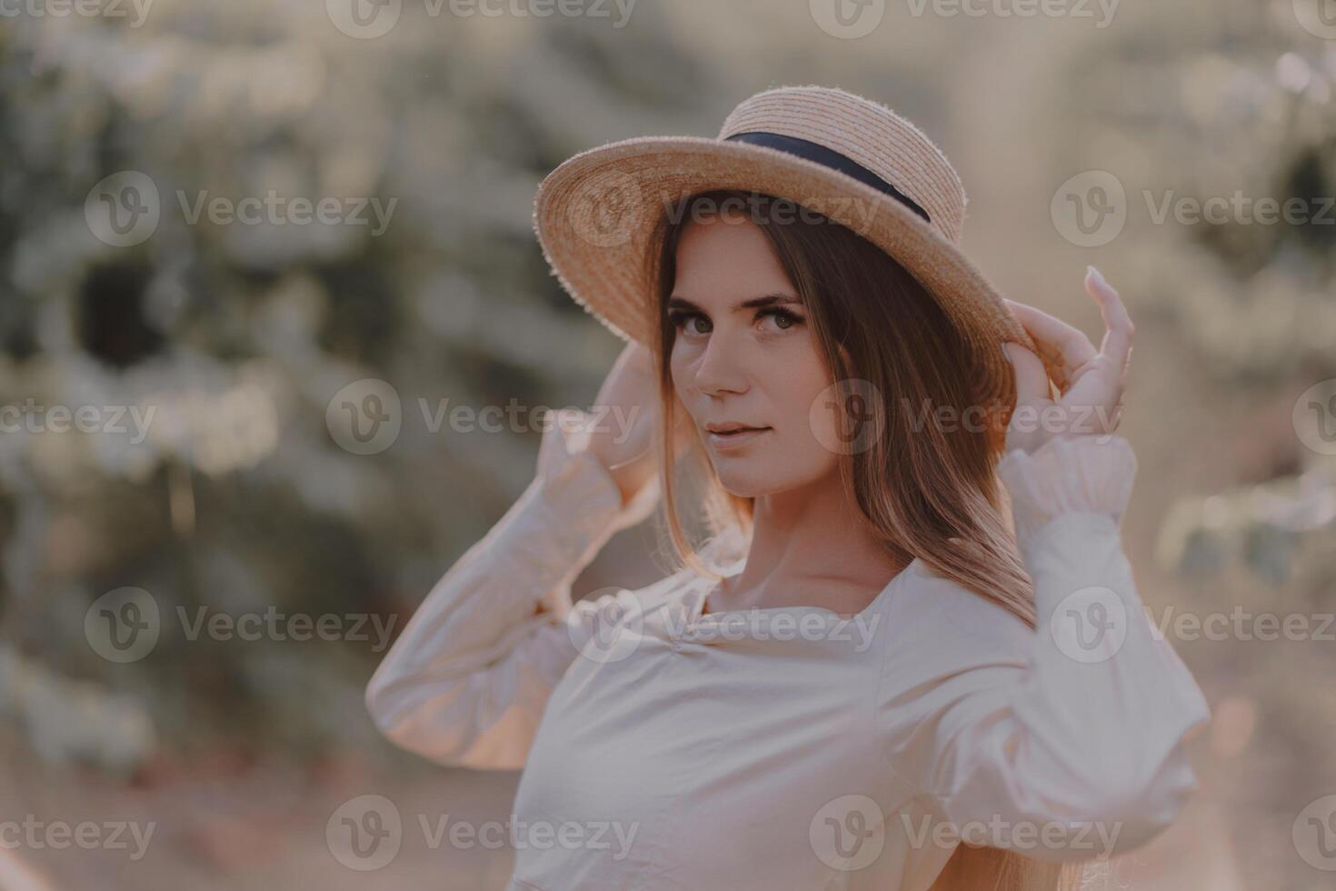 Woman with straw hat stands in front of vineyard. She is wearing a light dress and posing for a photo. Travel concept to different countries photo