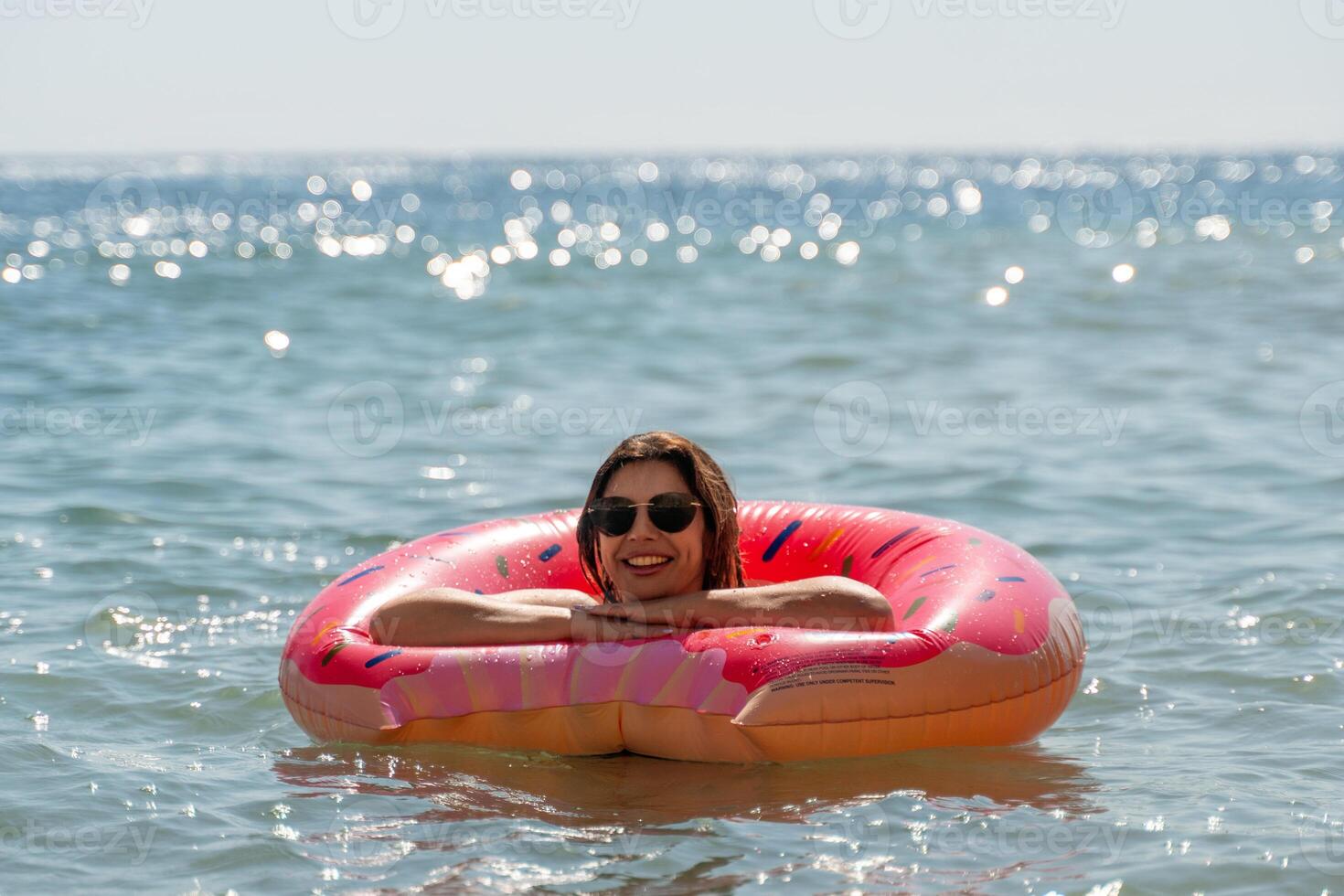 Woman, Float, Beach - Smiling Woman Relaxing on a Pink Inflatable Float in the Ocean on a Sunny Day. photo