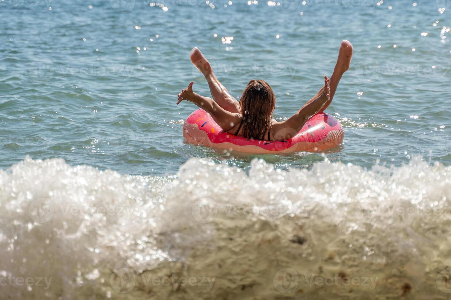 Woman, Beach, Float - A woman enjoys a sunny day by floating on a pink inflatable tube in the ocean. photo