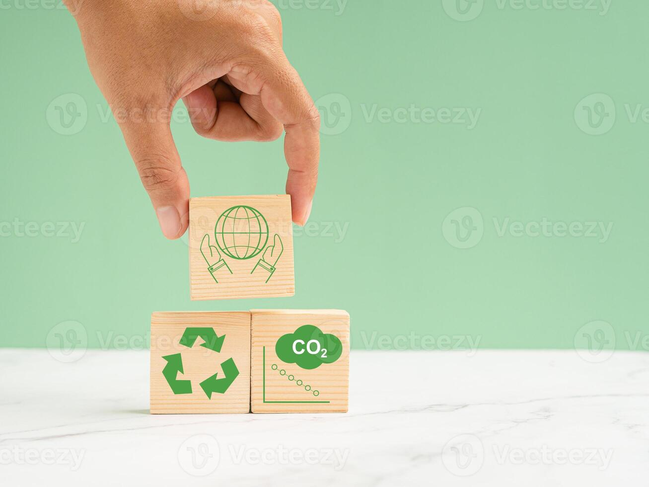 Net-zero greenhouse gas emissions target. Hand holding of a wooden cube with green icons over a marble floor against a light green background photo