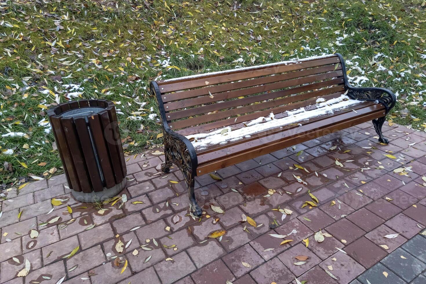 wooden bench in the park with a trash can and fallen leaves photo