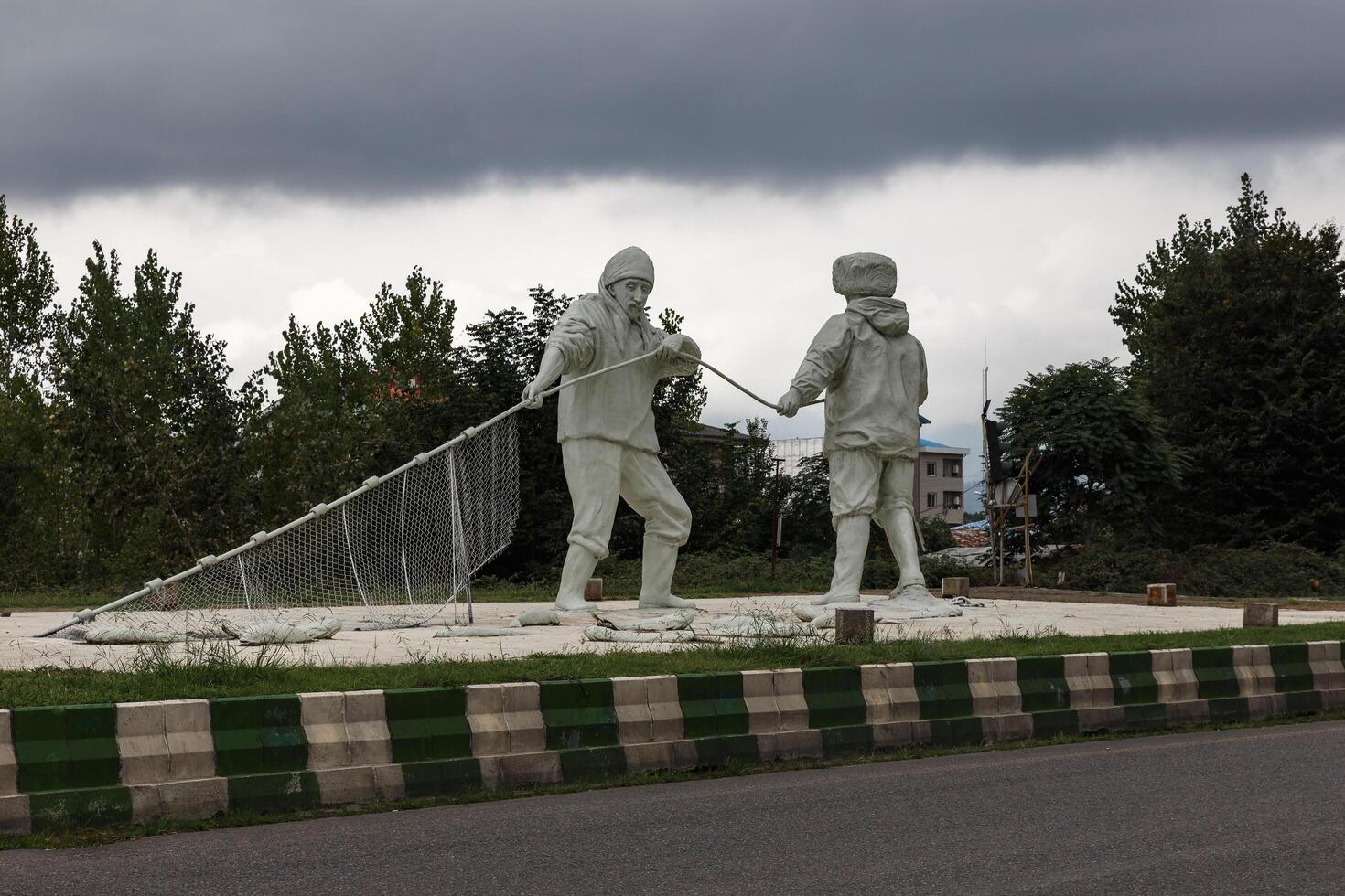 Paresar, Gilan Province, Iran - September 25, 2024 Two statues of men holding a fishing net. A statue of fishermen near the highway. photo