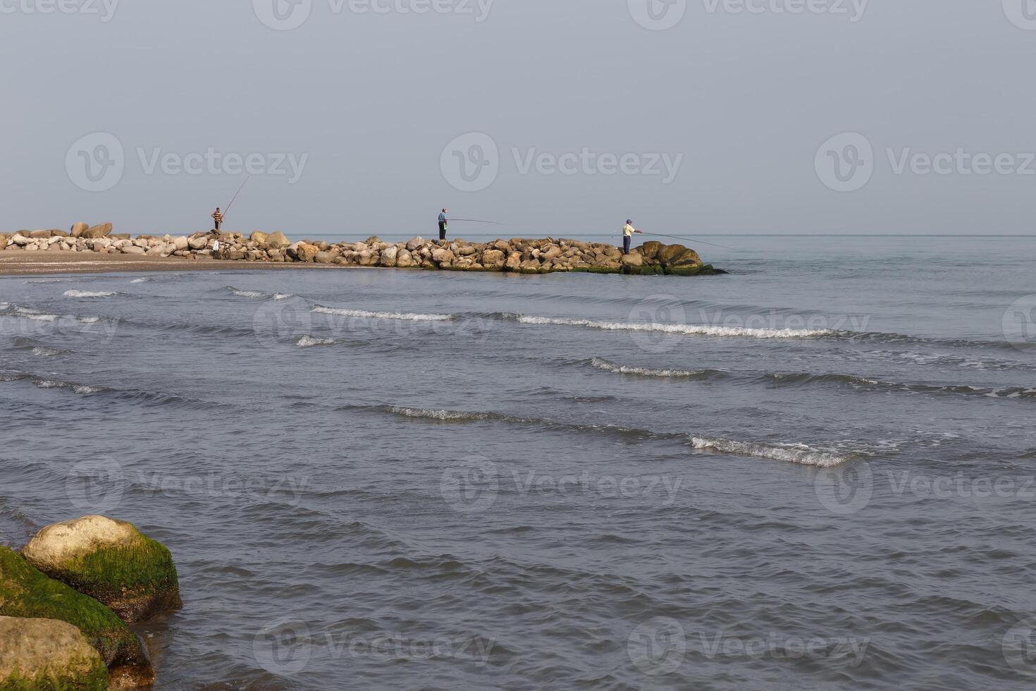 Fishermen stand on the shore and catch fish with a fishing rod. Caspian Sea, Iran photo