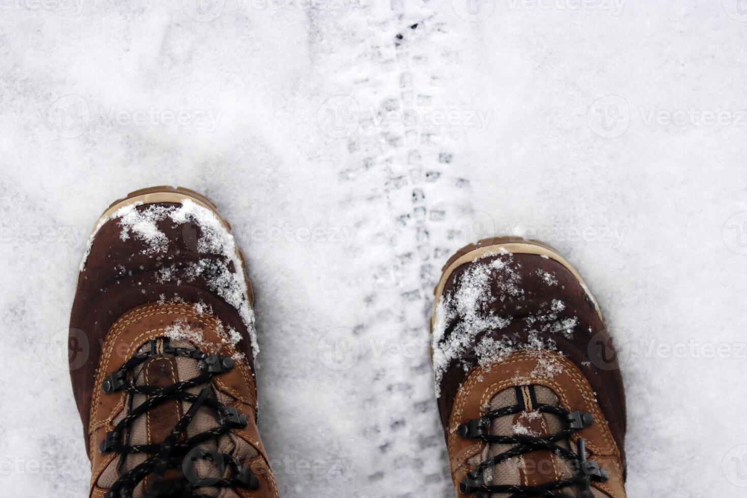 Pair of snow dusted boots standing near a tire tread on a snowy ground, capturing a moment of outdoor winter exploration and adventure. Copy space photo