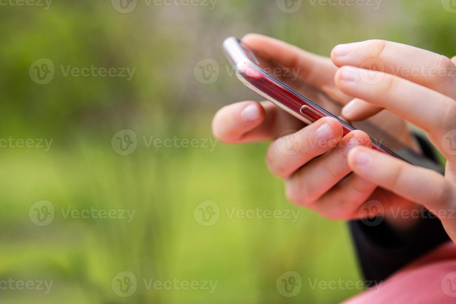 Closeup of a hand holding a mobile phone an outdoor setting. Teenager girl using smartphone, texting or browsing. Mobile technology in daily life. Modern lifestyle. Selective focus. Copy space photo