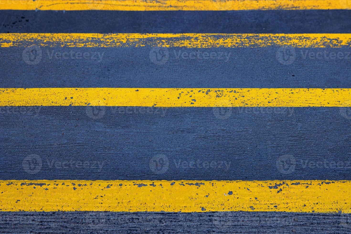 Closeup of a textured asphalt road with weathered yellow stripes on a rough gray pavement, great for use in street photography, urban design, or traffic-related visuals. Copy space photo