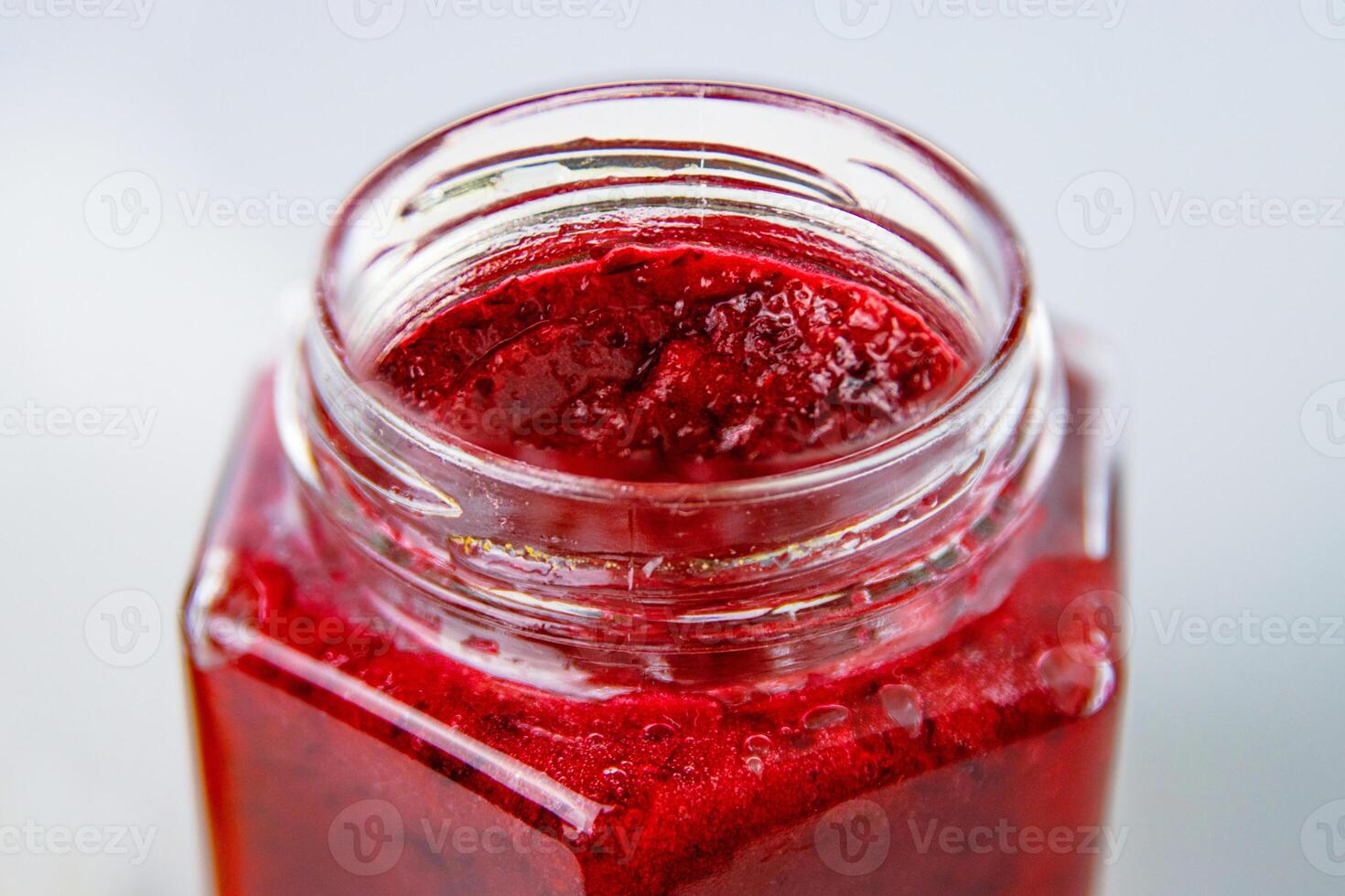 Fresh, vibrant red currant berry jam in an open glass jar, perfect for breakfast spreads or desserts. Closeup. Copy space. photo