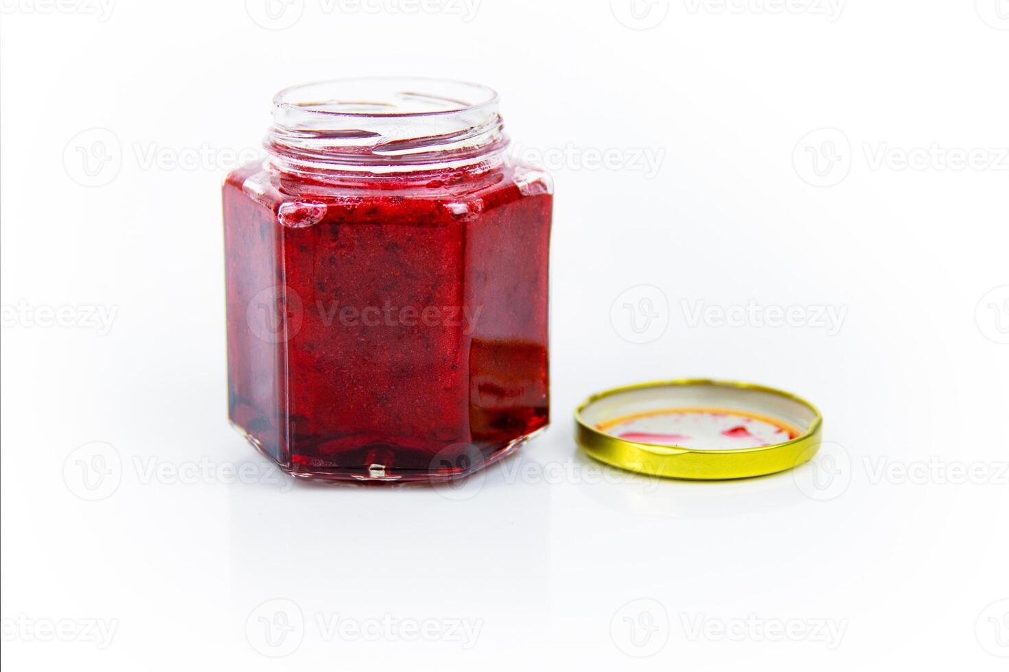 An open hexagonal glass jar of homemade red currant berry or cranberry jam with a gold lid beside it. Freshly made wild berries jelly. Copy space. Isolated on white background. photo