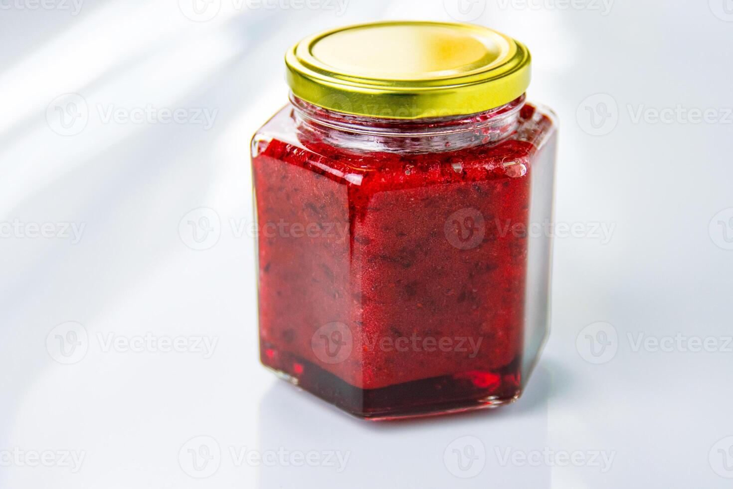 A hexagonal glass jar of homemade red currant berry or cranberry jam sealed with a gold colored metal lid. Freshly made wild berries jelly. Copy space. photo