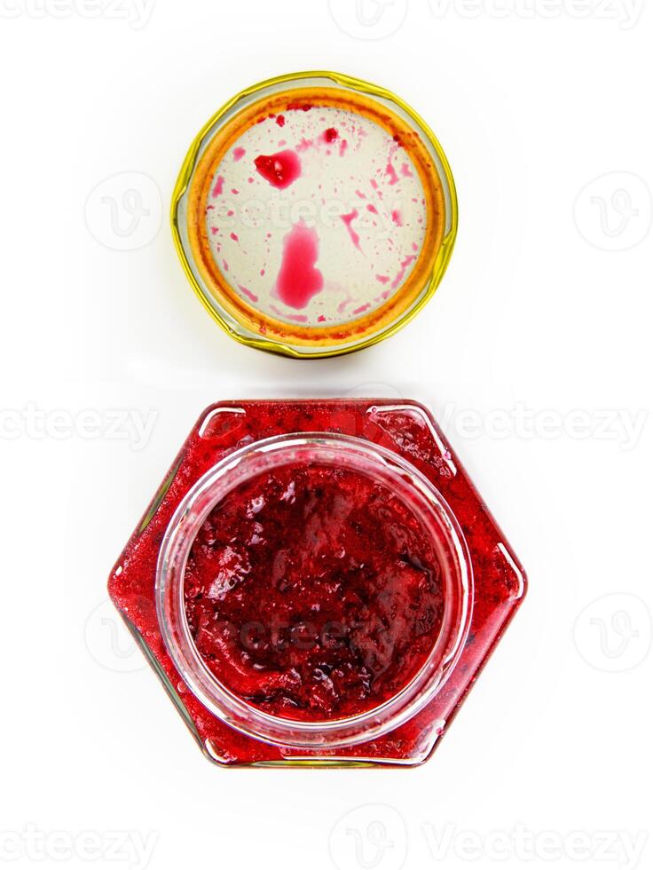 An open hexagonal glass jar of homemade red currant berry or cranberry jam with a gold lid beside it. Freshly made wild berries jelly. Copy space. Isolated on white background. Top view photo