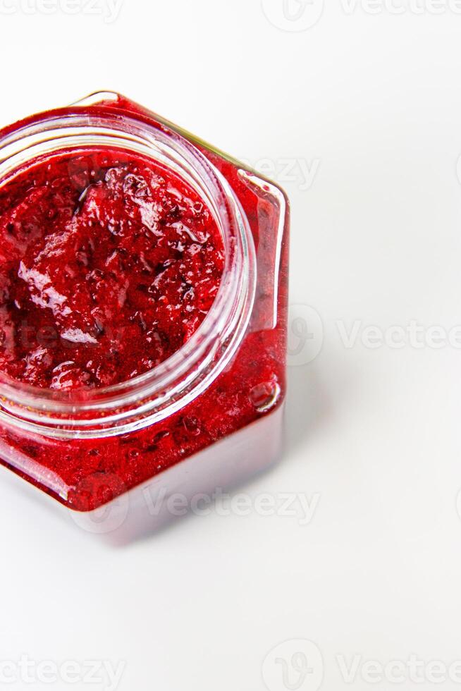 Crop top view of fresh, vibrant red currant berry jam in an open glass jar, perfect for breakfast spreads or desserts. Closeup. Copy space. Isolated on white background. photo