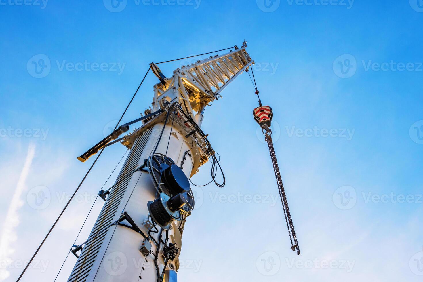 A large construction crane with cables extending against a clear blue sky, White crane arm and hanging cables captured from below, illustrating industrial work and heavy lifting. Copy space photo