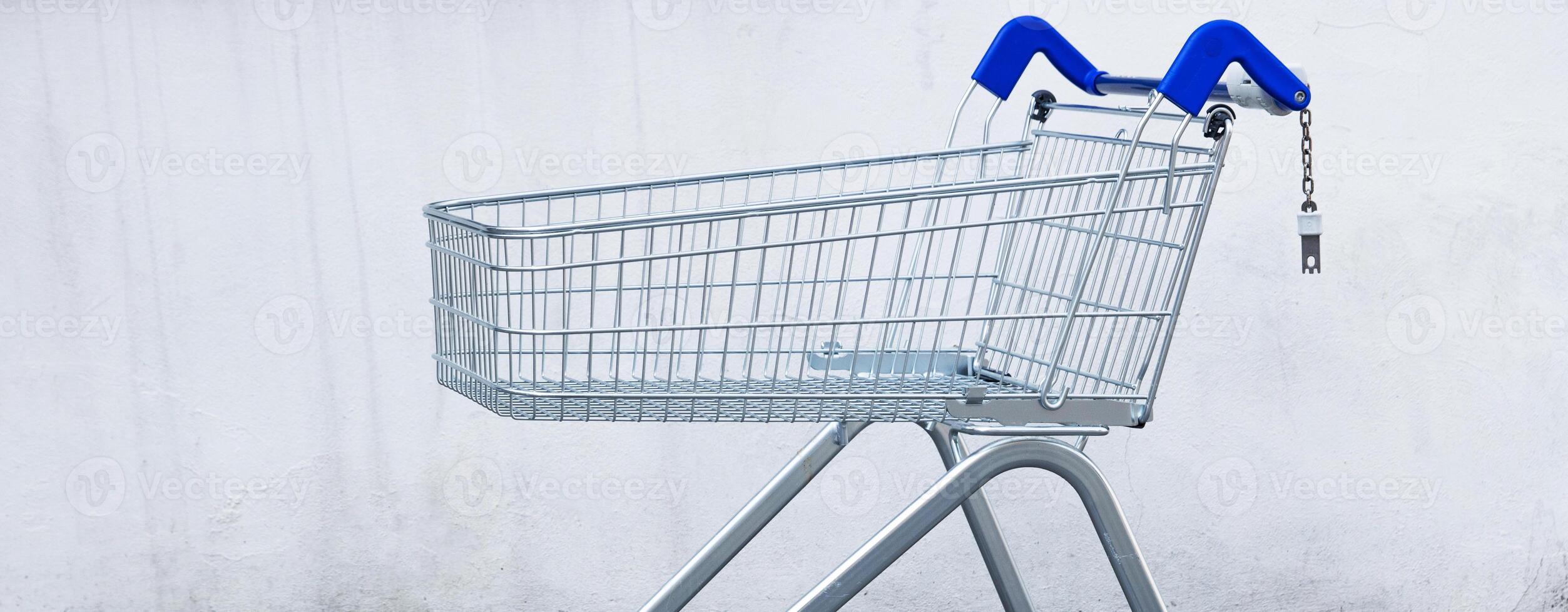 Empty metal shopping cart from supermarket against a white wall, ideal for retail and consumer shopping concepts. Copy space photo