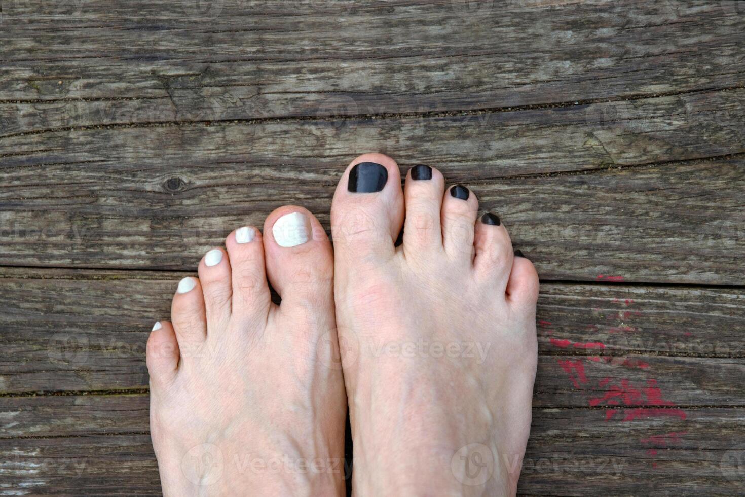 Bare feet with black and white painted toenails resting on the wooden floor. Two feet with contrasting nail polish, symbolizing individuality, personal style and relaxation. Copy space photo
