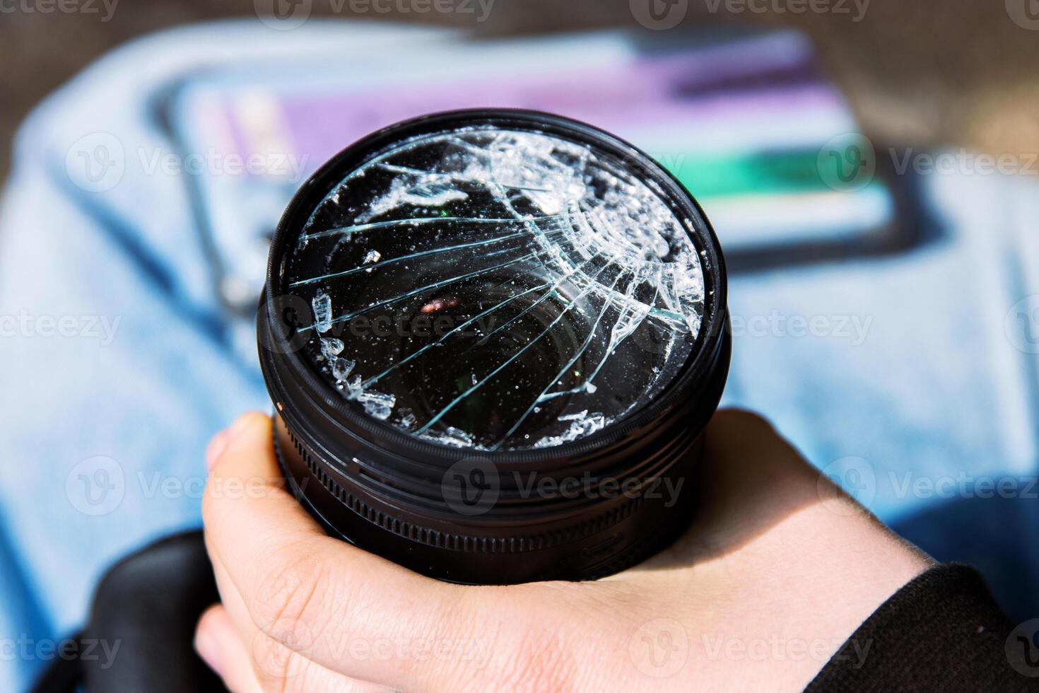Closeup of a hand holding a broken shattered camera lens with visible cracks, symbolizing damage and fragility of photography equipment, repair or replacement needs, accidents, or fragility. photo