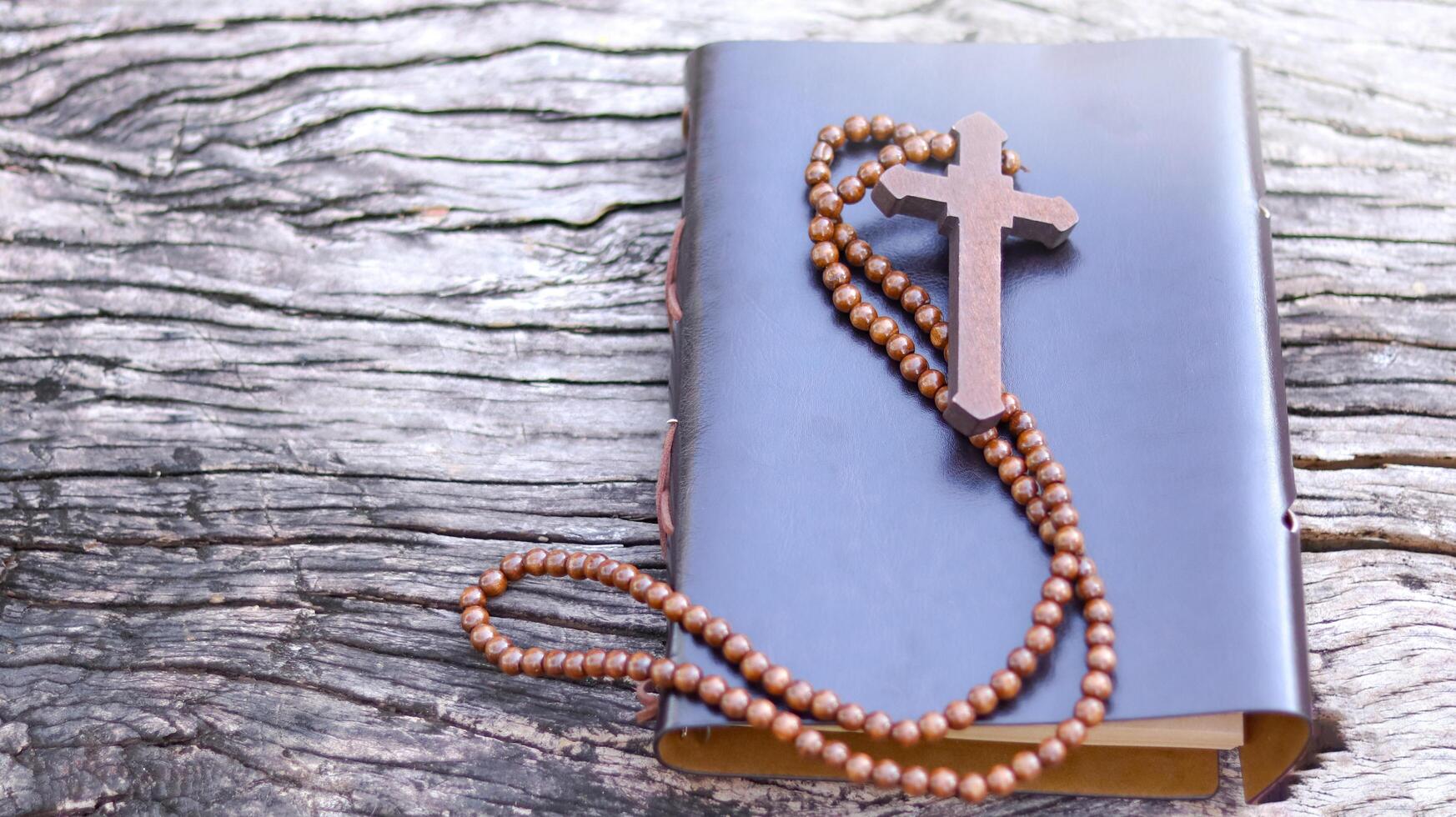 Dark red wooden cross on a book cover on wooden background symbolizing the spread of Jesus Christs love among Christians reflecting faith devotion and the importance of Christian teachings. photo